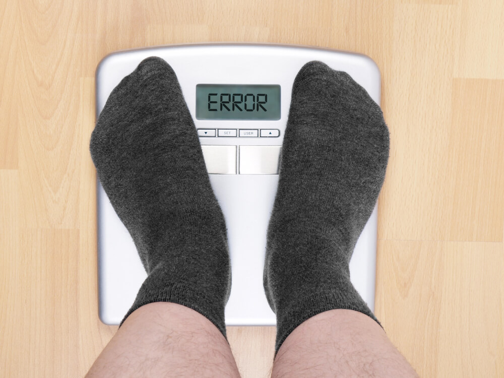 Feet wearing gray socks stand on a scale that displays an error