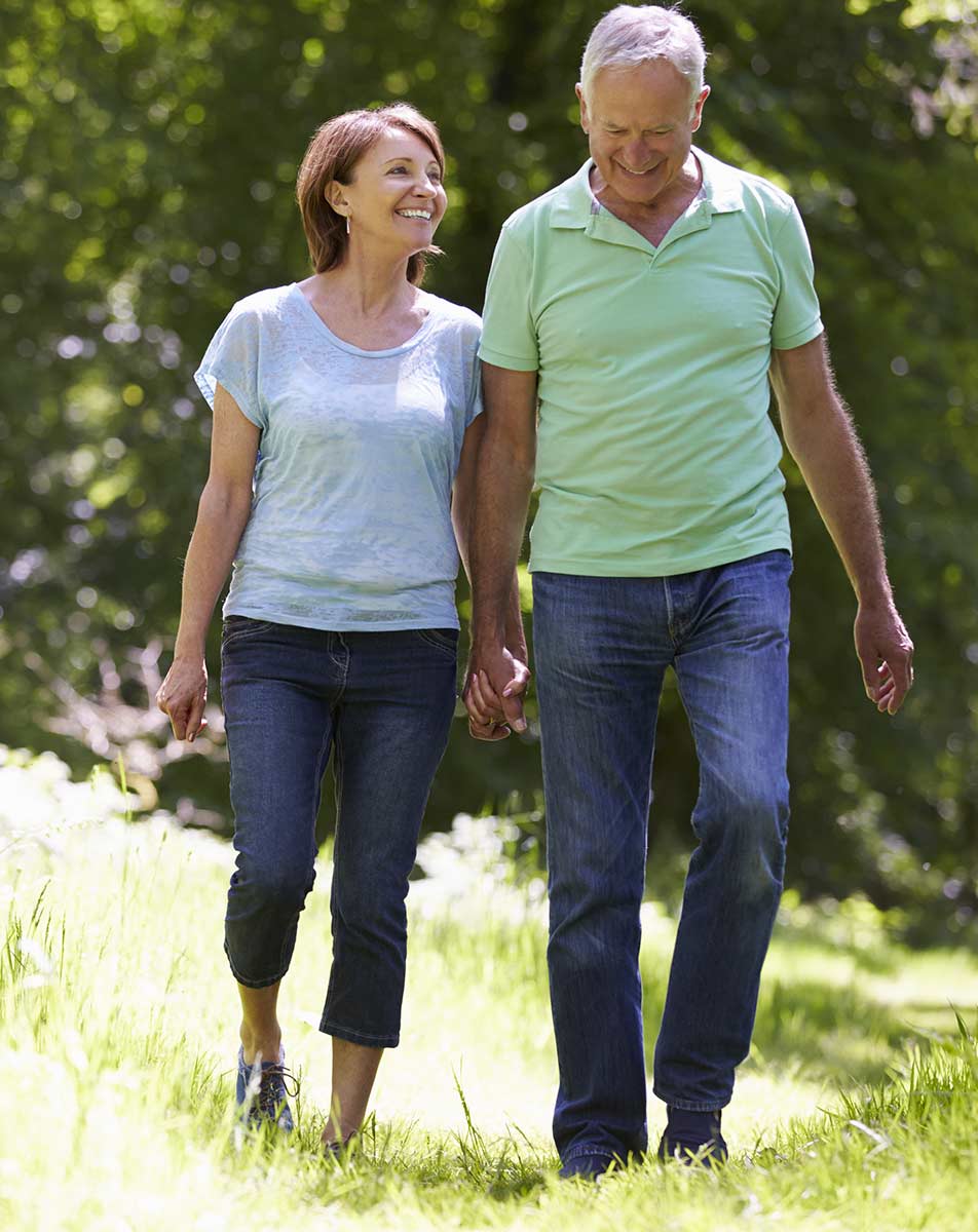Smiling elderly couple holding hands while walking on grass