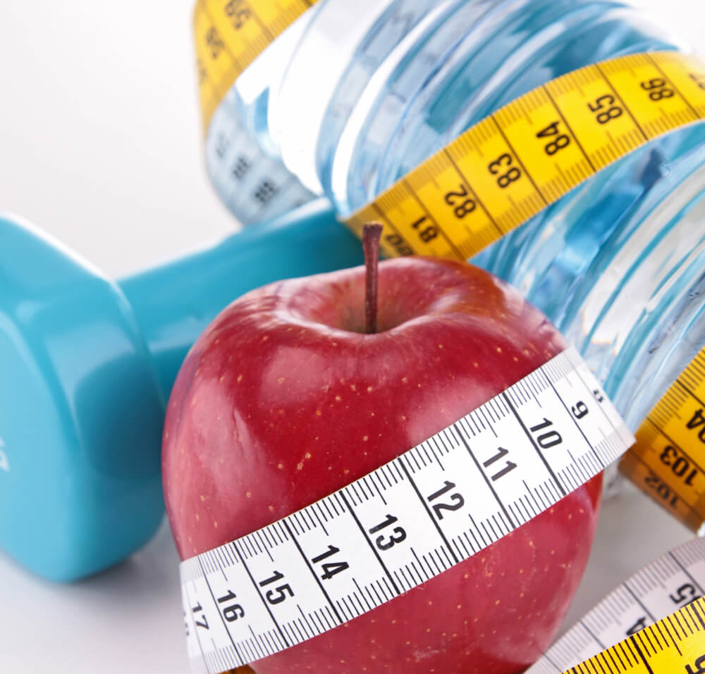 A bottle of water, a red apple, and a hand weight wrapped in measuring tape