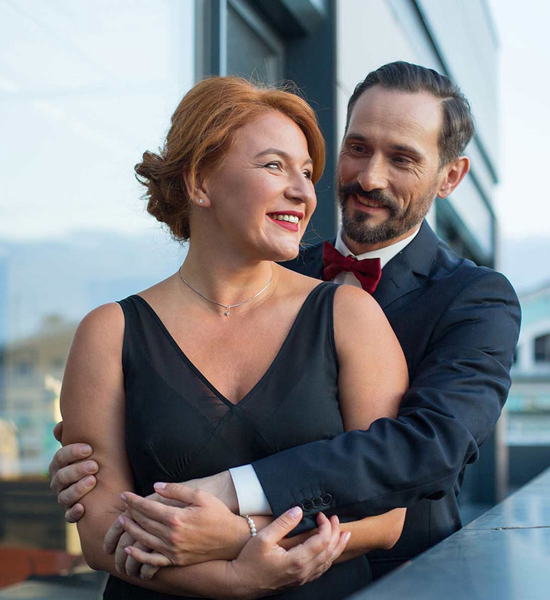 A man and woman in formal attire embrace on a balcony