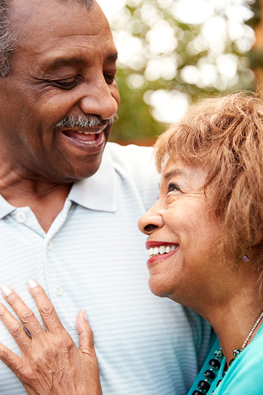 A smiling woman looks up at her smiling husband sweetly with a hand on his chest