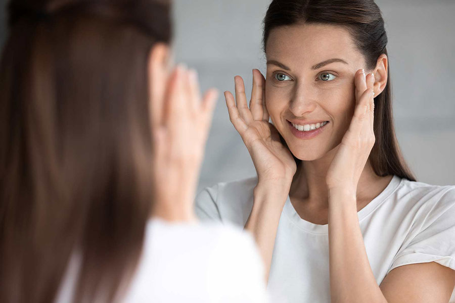 A woman examining her microneedling results in the mirror