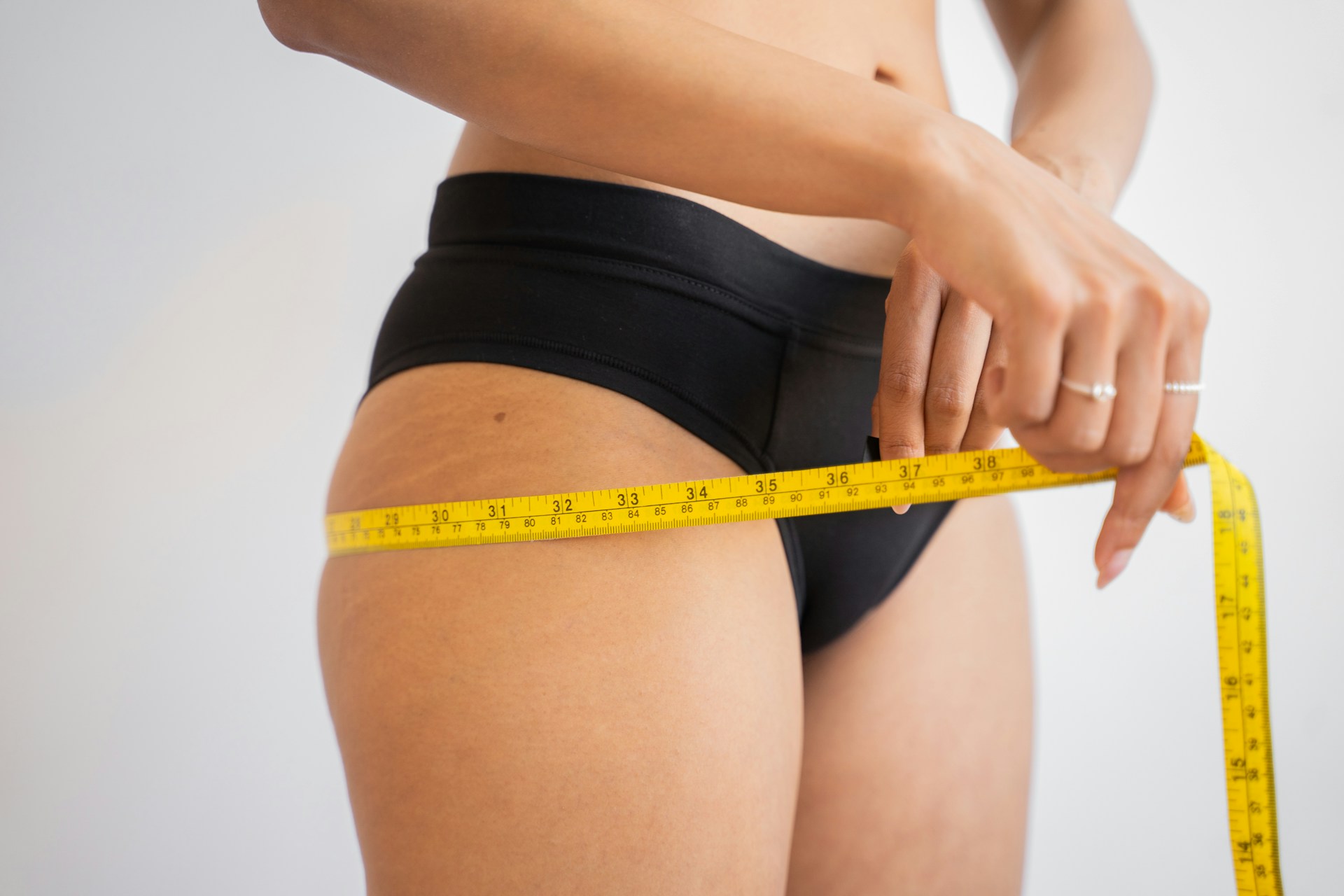 A woman measures her thigh with a yellow measuring tape