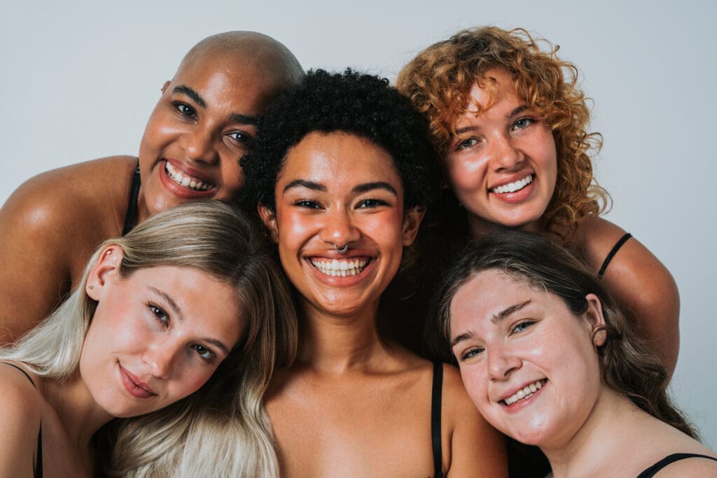 A group of five diverse smiling women with glowy, rejuvenated skin