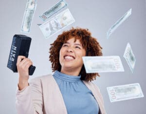 A smiling woman holds a money gun as several one hundred dollar notes rain down around her File Name: make-it-rain-money