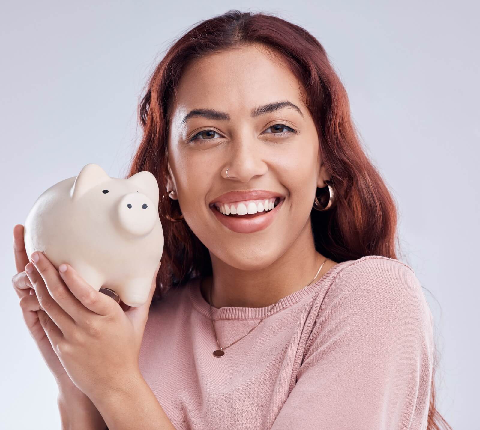 A smiling woman in a pink sweater holds a piggy pank close to her face