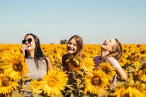 Three women laugh together in a field of sunflowers