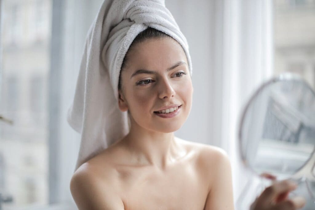 Woman wearing a towel on head smiling at her reflection in a hand mirror