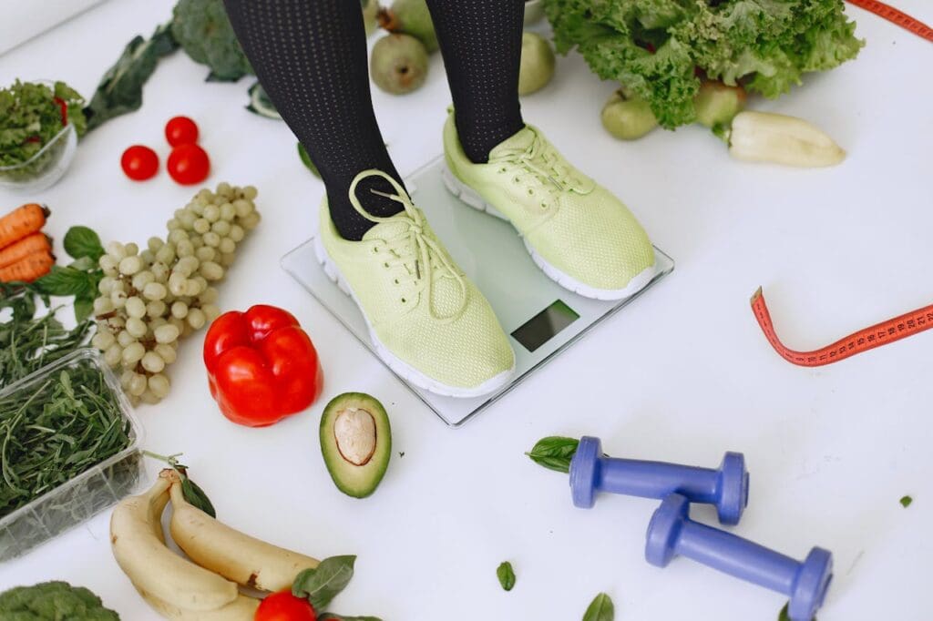 Person standing on scale surrounded by vegetables and dumbbells