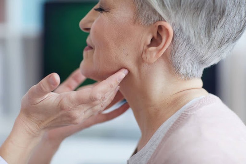 The hands of a doctor examining the tight neck of a happy woman