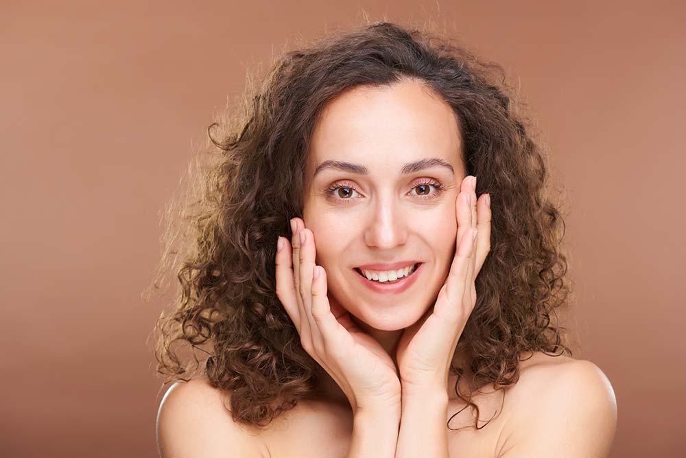 A smiling brunette woman cradles her clear, radiant face