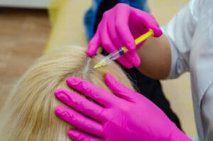 A professional wearing pink gloves injects a woman’s scalp with PRP