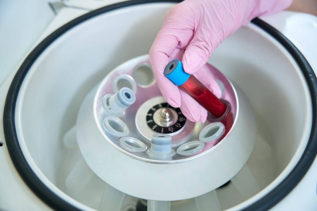 A tube of blood being placed in a centrifuge by a gloved hand