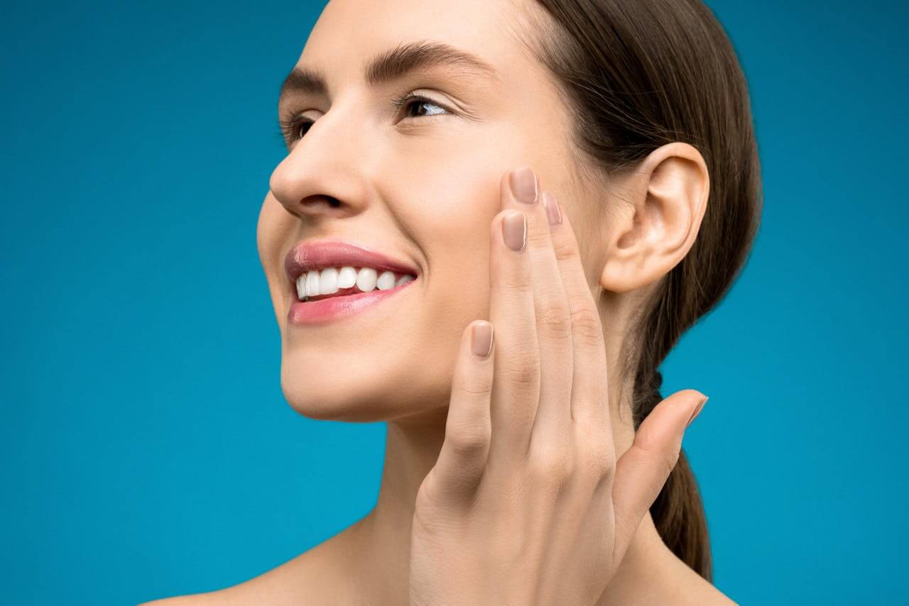 A smiling woman touches her glowing face