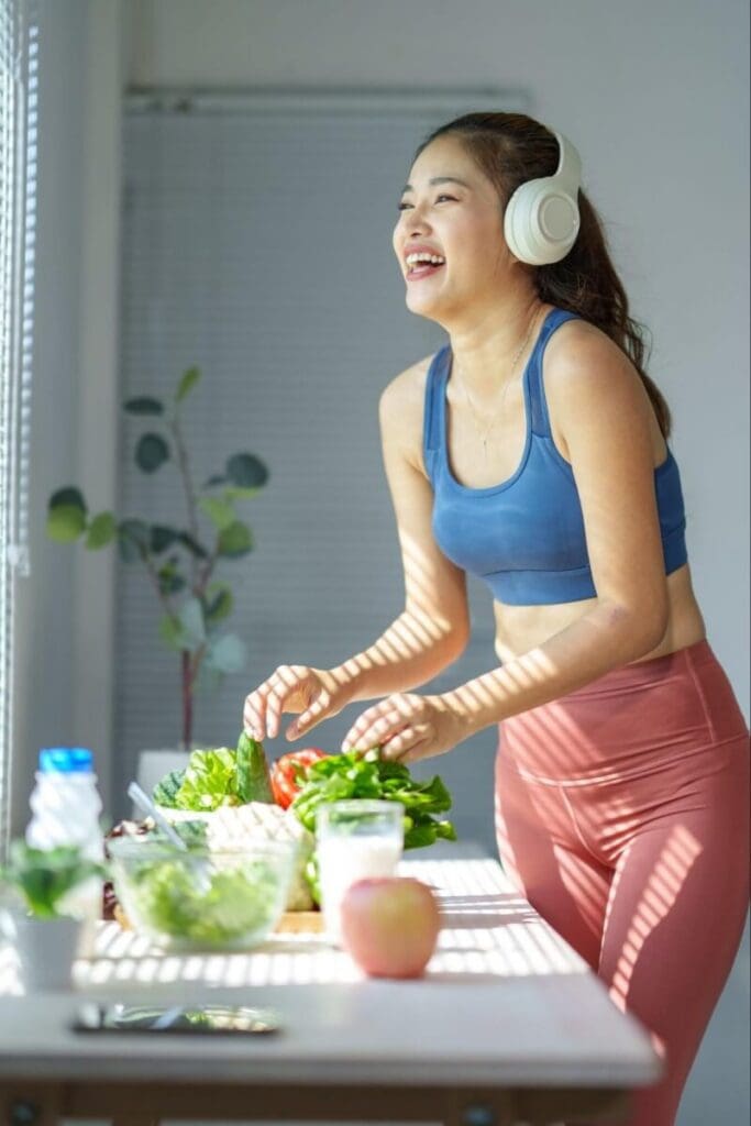 A happy young woman wearing headphones preps fresh vegetables
