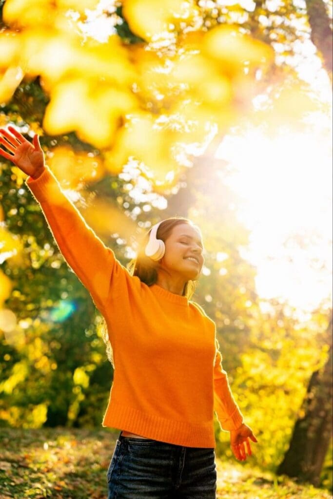 A woman in orange wearing headphones enjoys a sunny afternoon in nature