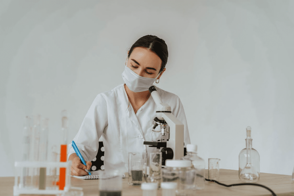 Scientist surrounded by lab equipment, wearing a face mask, and writing notes