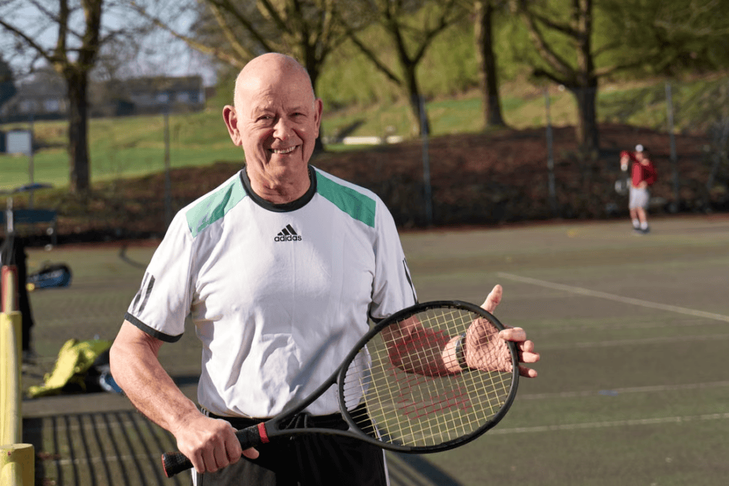 A smiling older man holding a tennis racket